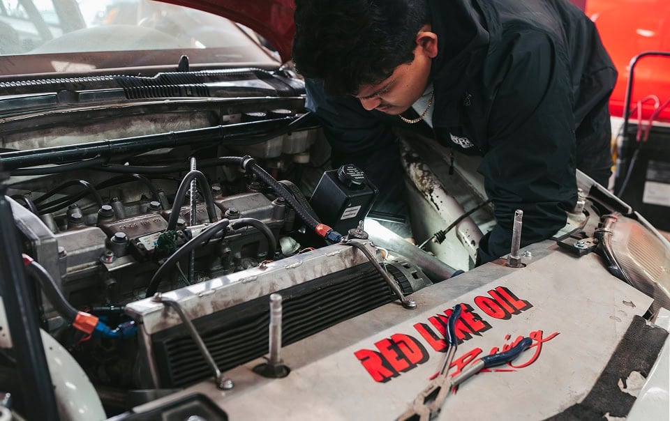 Young mechanic working on car engine at Black Market Racing workshop.