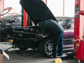 Mechanic working on a black sports car in a garage.