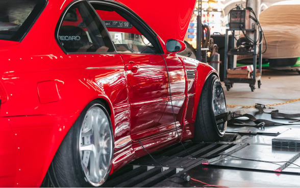 Red modified racing car on dynamometer for performance testing.