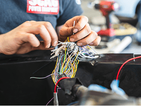 Technician repairing complex wiring for Black Market Racing vehicle.