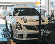 White Cadillac racing car in workshop with tools and equipment around.