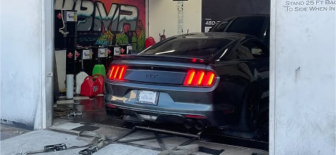 Black Ford Mustang GT with racing stripes in garage, custom modifications visible.