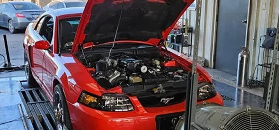 Red Ford Mustang at Black Market Racing workshop with open hood.