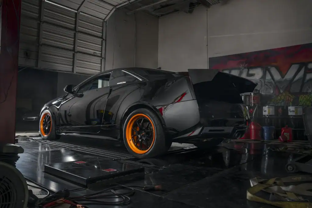 Matte black sports coupe on orange wheels strapped to the dyno at Black Market Racing
