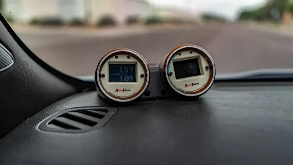 Two automotive digital gauges on dashboard during dyno tuning session.