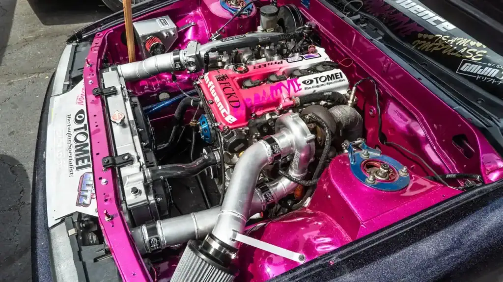 Pink engine bay with a turbocharged four-cylinder, Tomei valve cover and polished intake piping