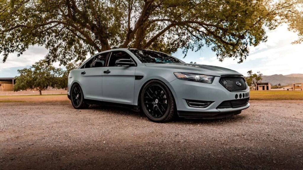 Matte grey Ford Taurus SHO on black wheels, parked under a tree
